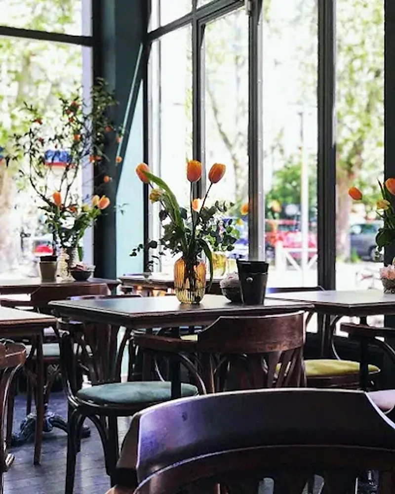 La sala di Biffi con le grandi vetrate: tavolini scuri, sedie in legno e tulipani in un vaso