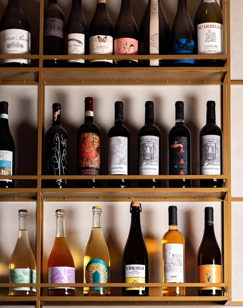 La parete dei vini di Biffi: bottiglie di etichette piemontesi, toscane e vini naturali su scaffali dorati
