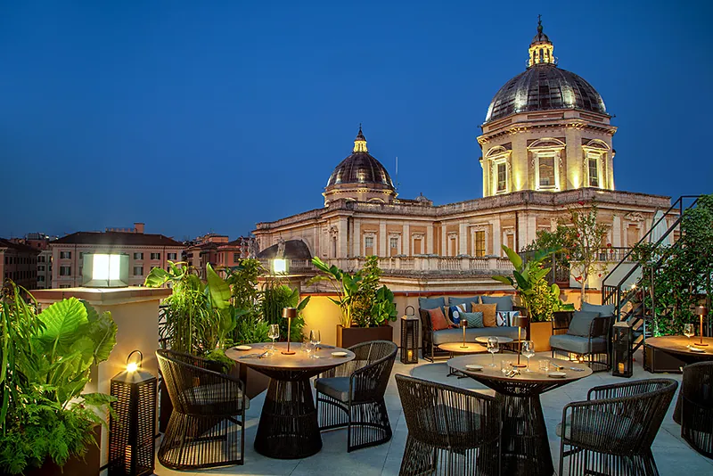 La terrazza di Masa Roof Top all'ora blu, con i tavoli tra le piante e le cupole illuminate di Santa Maria Maggiore