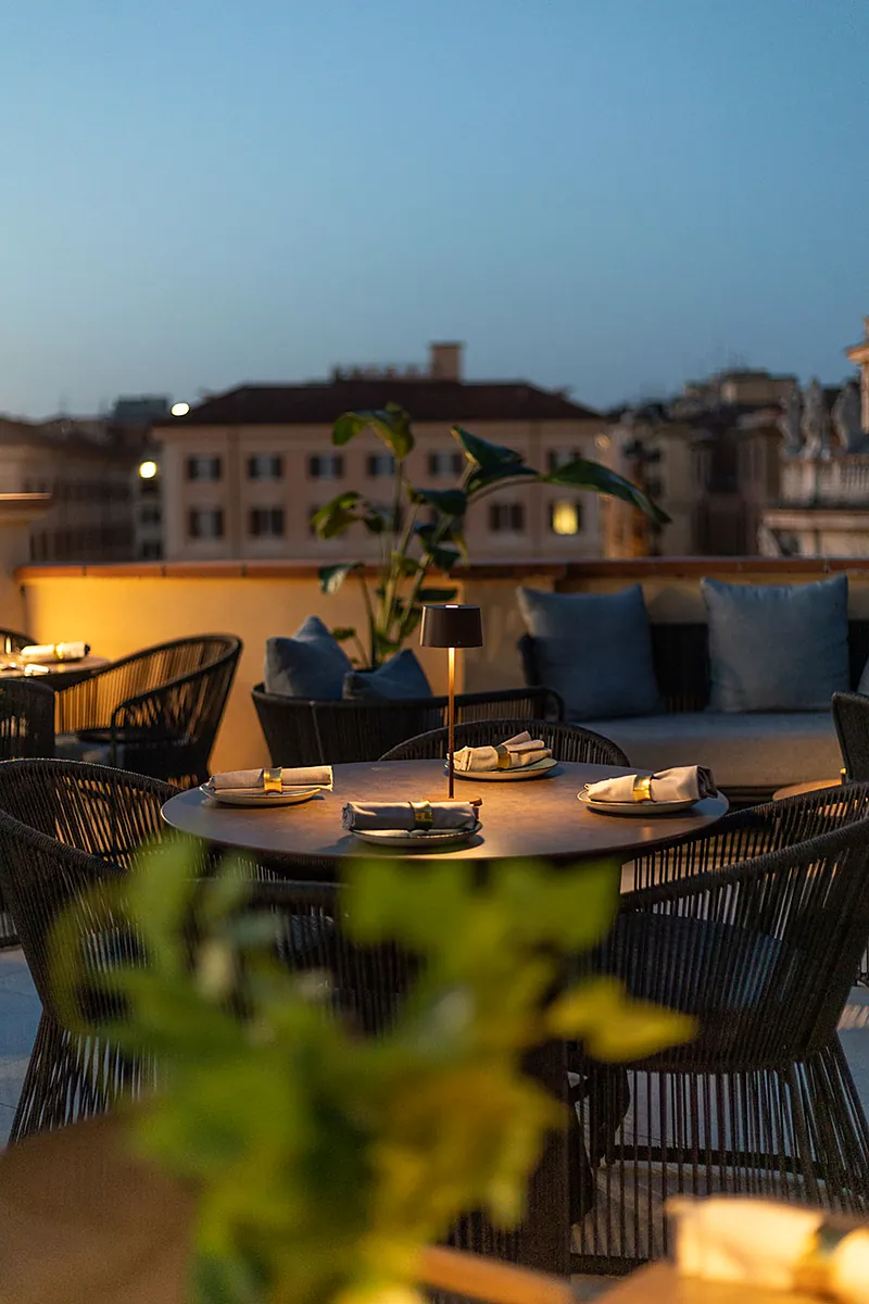 Un tavolo apparecchiato sulla terrazza di Masa Roof Top all'imbrunire, con i palazzi di Monti sullo sfondo