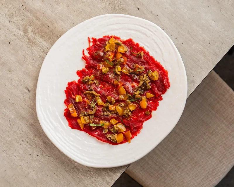 Carpaccio di carne condito su un piatto bianco