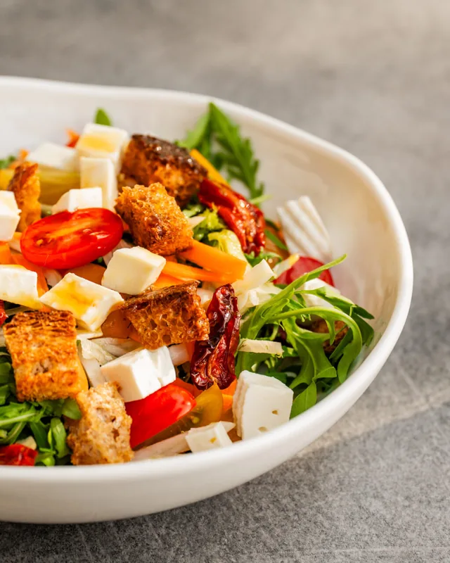 Insalata con formaggio, crostini, pomodorini e rucola in una ciotola bianca