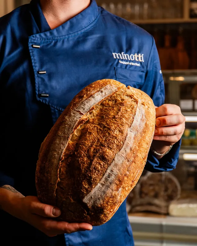 Un cuoco in giacca blu tiene in mano una pagnotta di pane fresco