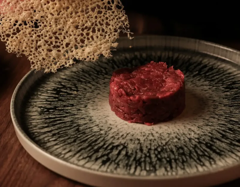 Tartare di carne su un piatto scuro, con una cialda croccante